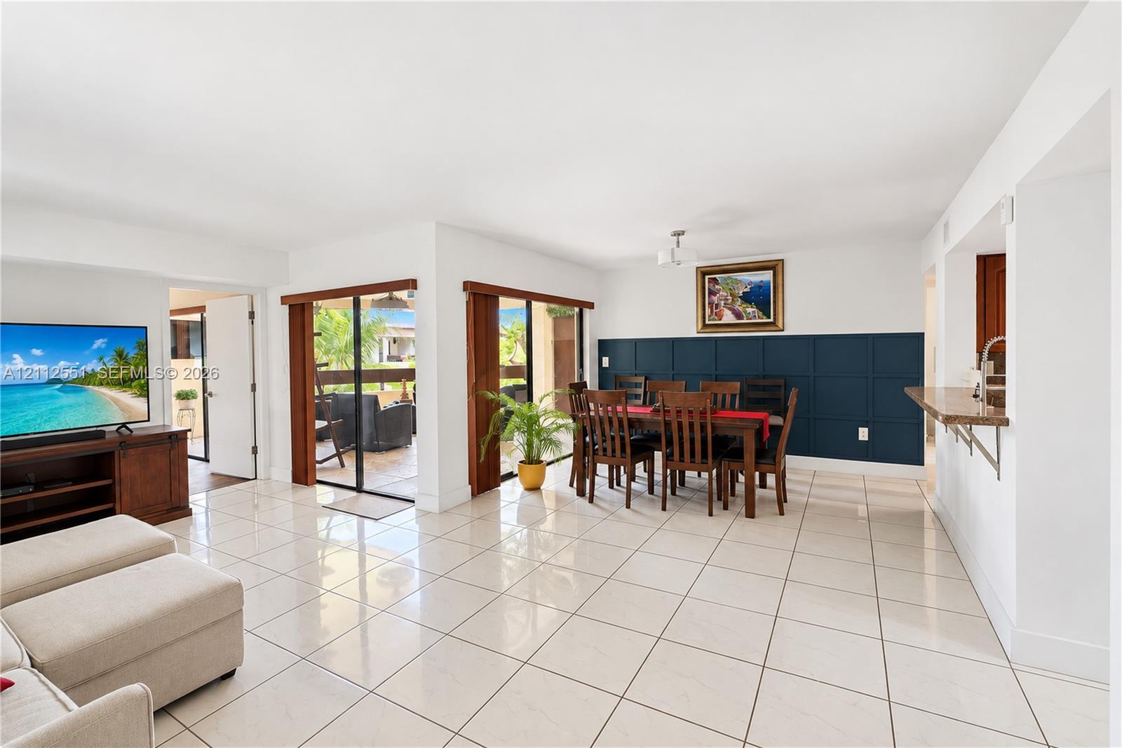 Large format ceramic tile flooring, dual sliding glass doors, and a deep-blue grid wainscoting accent wall, complemented by a kitchen pass-through counter Large format ceramic tile flooring, dual sliding glass doors, and a deep-blue grid wainscoting accent wall, complemented by a kitchen pass-through counter