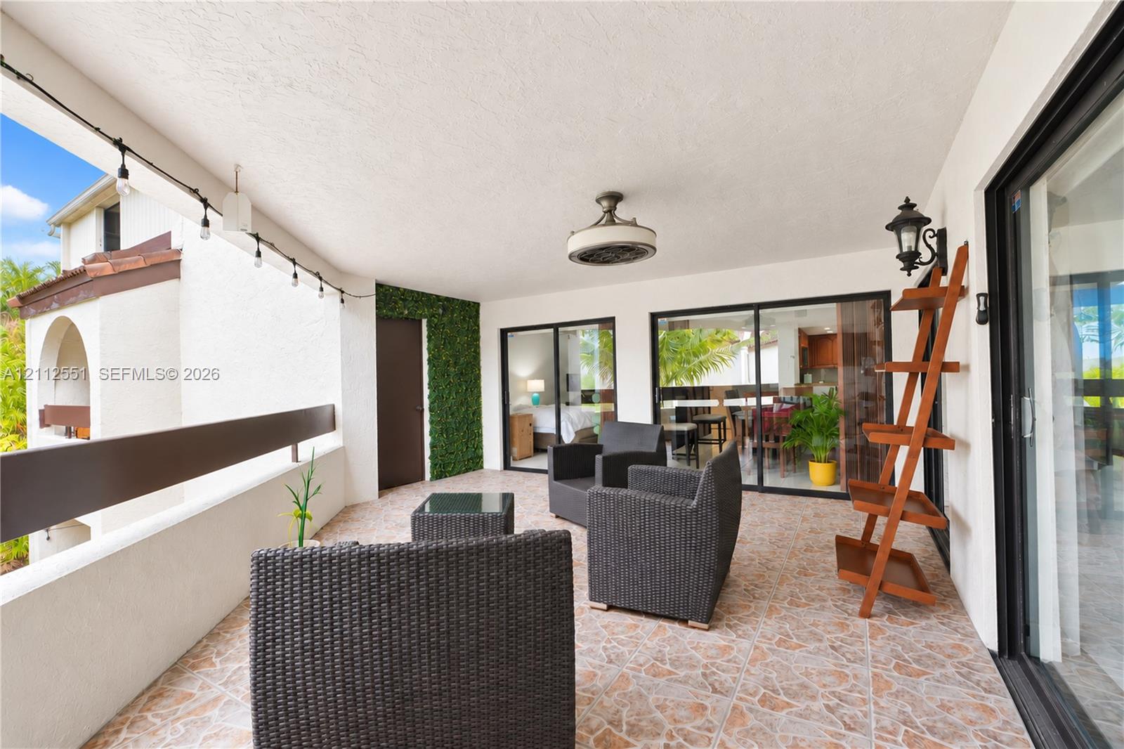 Covered balcony featuring multi-tonal tile flooring, a mounted ceiling fan, wall-mounted lantern-style lighting, and a green decorative wall accent