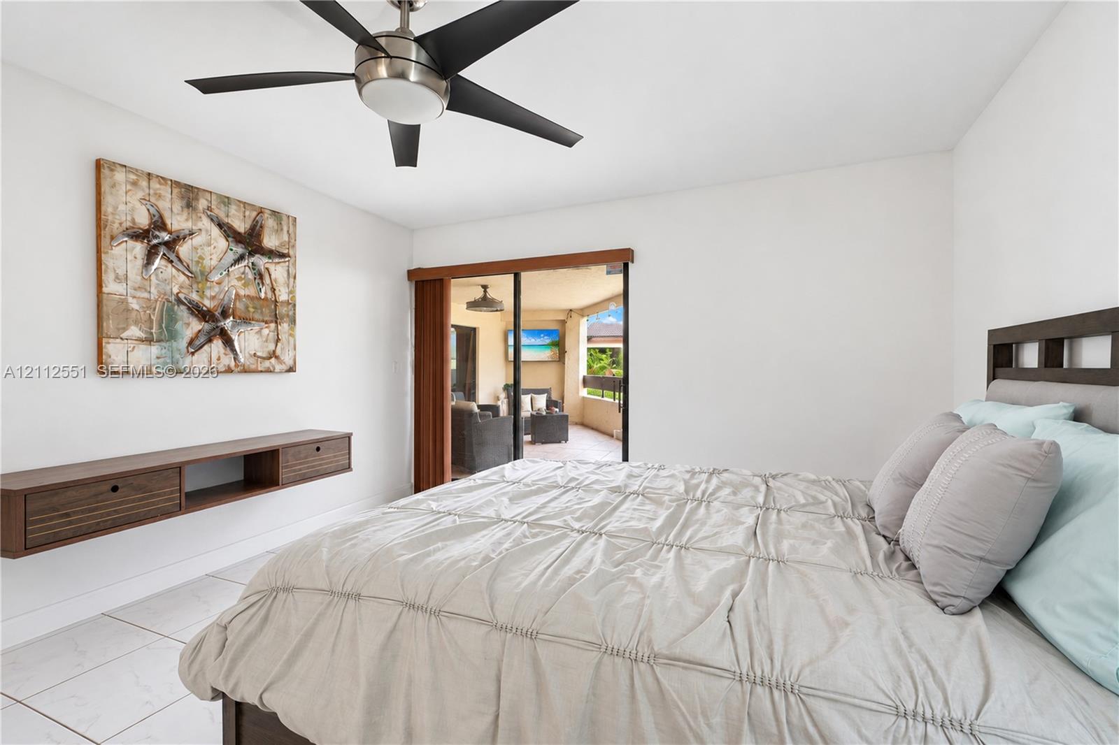 Large bedroom featuring tile flooring, a dual-tone wall-mounted storage console, and a brushed nickel ceiling fan with integrated lighting