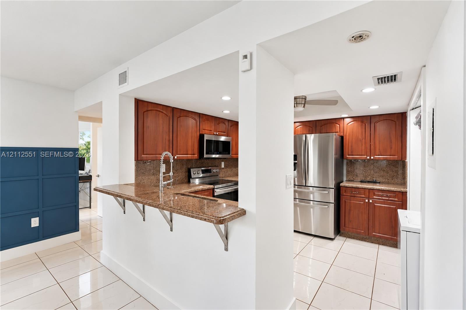 Kitchen featuring stained wood cabinetry, stone-surface countertops, breakfast bar, and stainless steel appliances, accented by tile flooring and blue paneled wall detailing