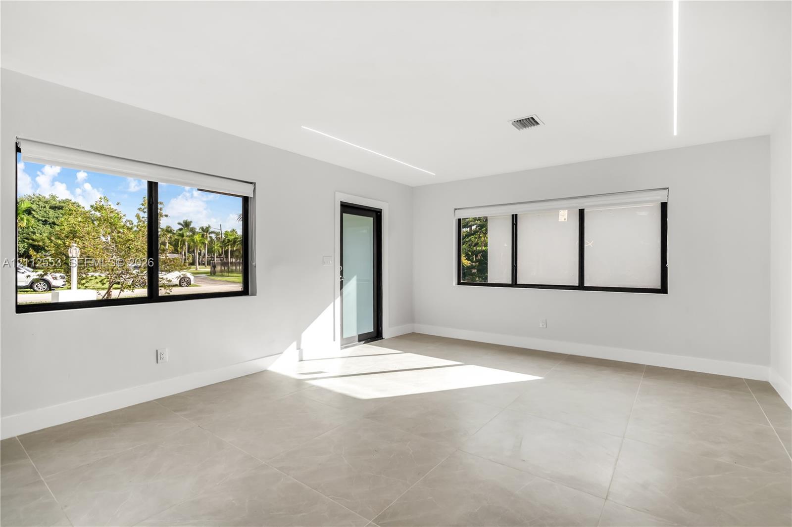 Interior space featuring large-format tile flooring, recessed linear ceiling lighting, black-framed windows with integrated shades, and a glass-paneled exterior door