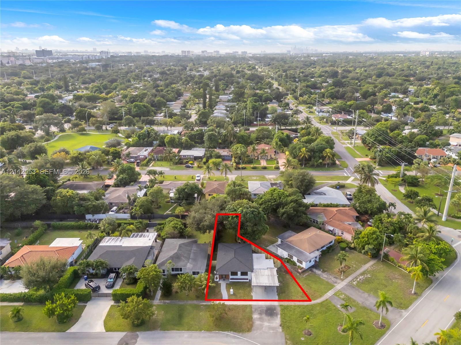 Aerial view of a residential property featuring a hipped roof, a concrete walkway, a covered parking structure, and mature landscaping within a corner lot