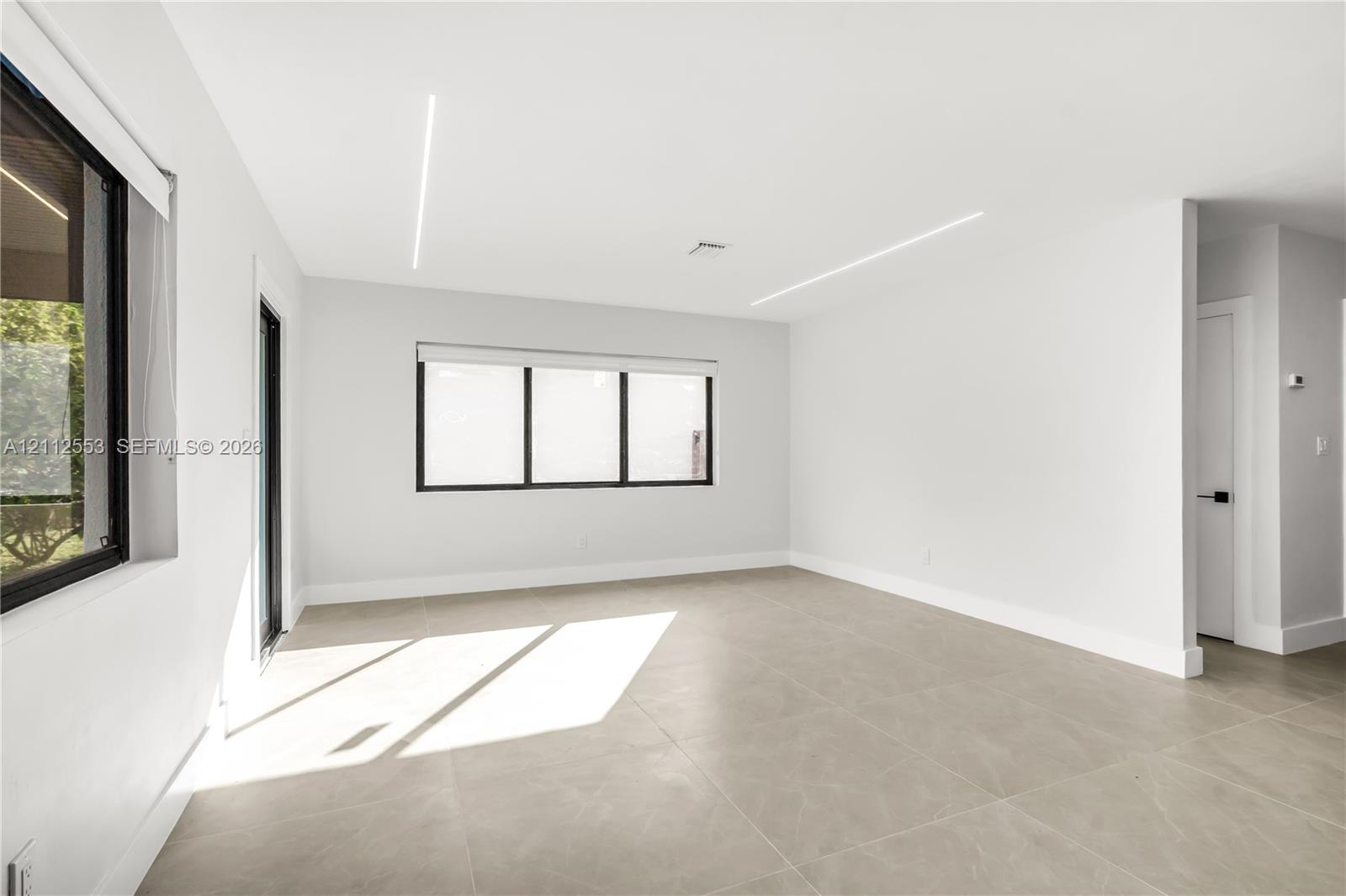 Neutral-toned tile flooring, recessed linear LED ceiling lighting, and black-framed windows