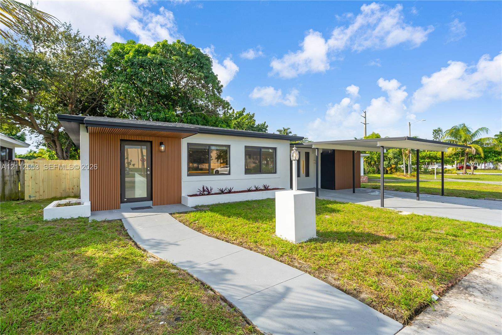 Mid-century modern exterior featuring vertical wood siding accents, low-slope roofline, concrete walkway, and an attached covered carport