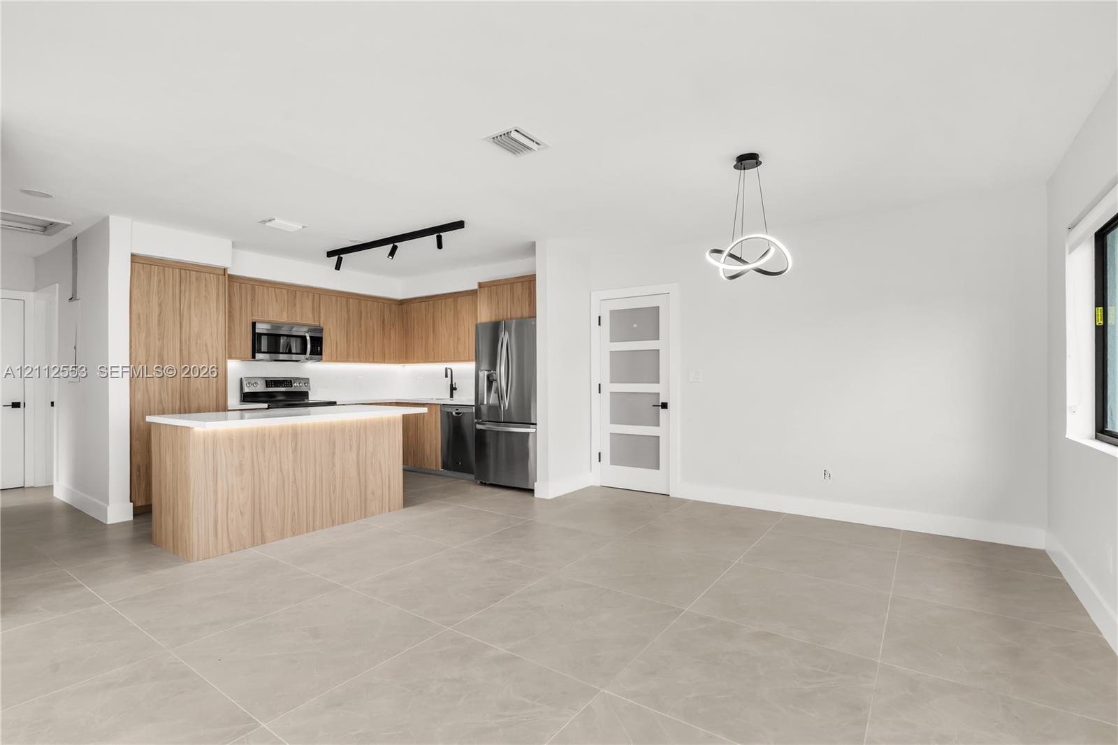 Kitchen featuring wood-finish cabinetry, a central island with a quartz countertop, stainless steel appliances, matte black track lighting, and large-format tile flooring