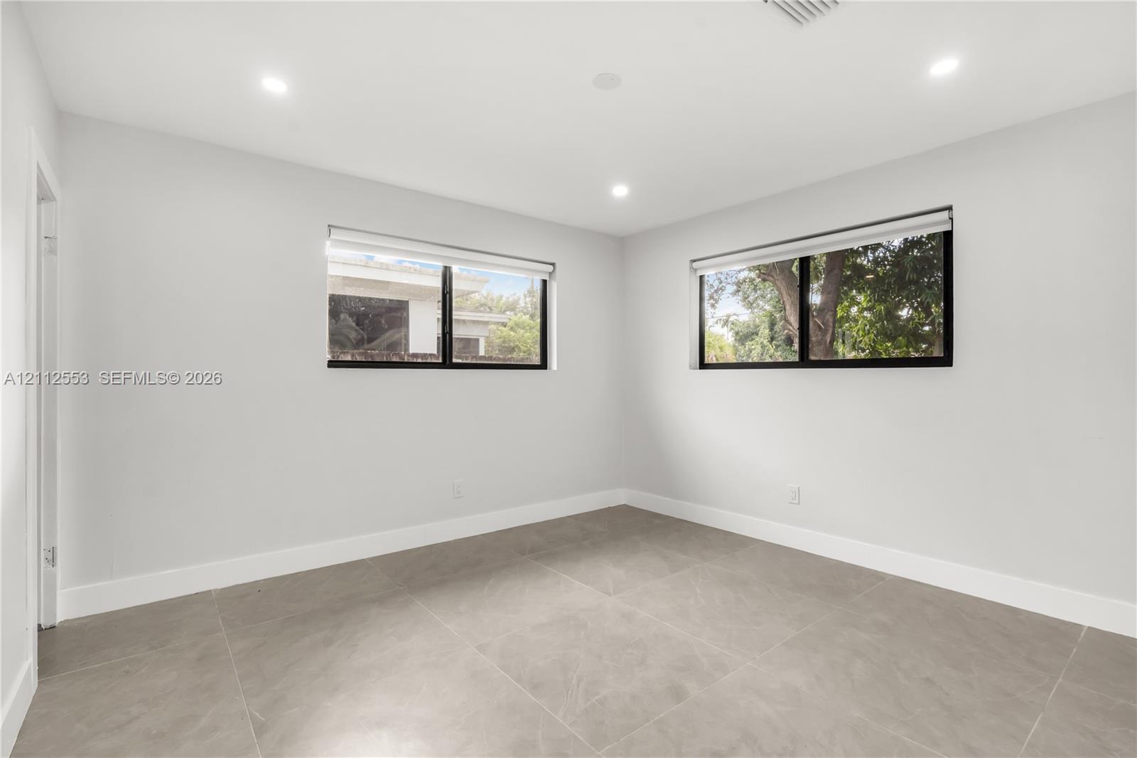 Neutral-toned room featuring large-format tile flooring, dual windows with black frames, recessed ceiling lighting, and smooth-finish walls