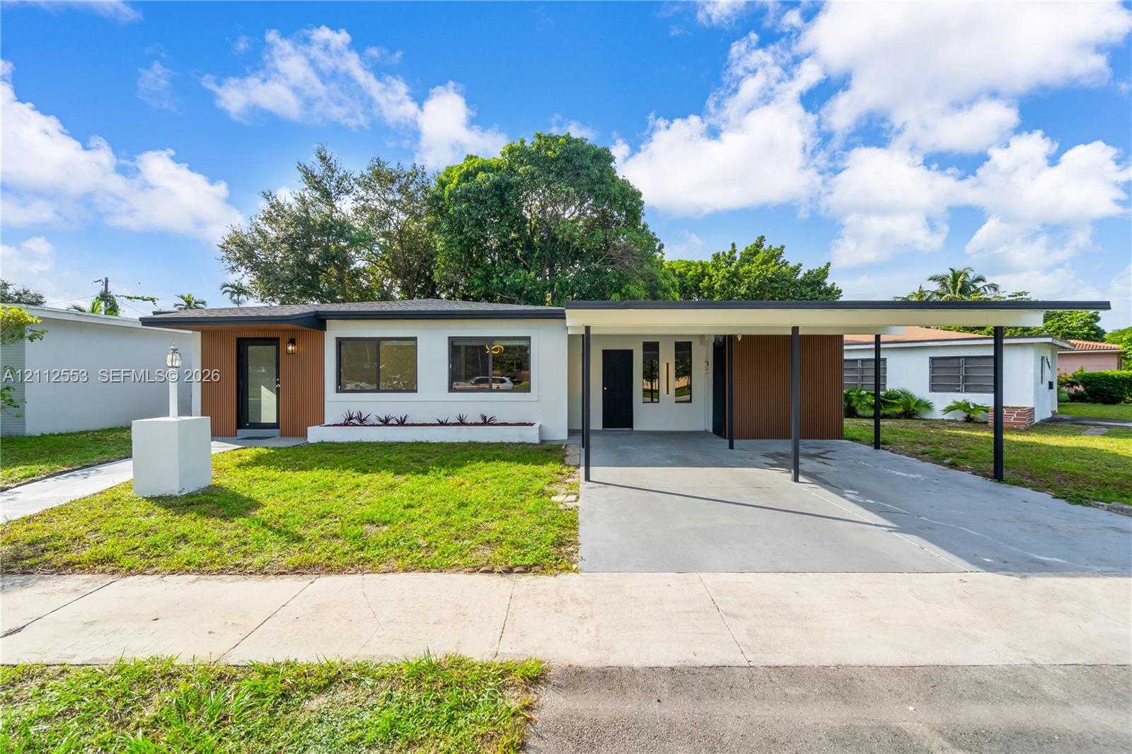 Mid-century modern exterior featuring wood-tone paneling, white stucco facade, flat roofline, and attached carport with metal support columns Mid-century modern exterior featuring wood-tone paneling, white stucco facade, flat roofline, and attached carport with metal support columns