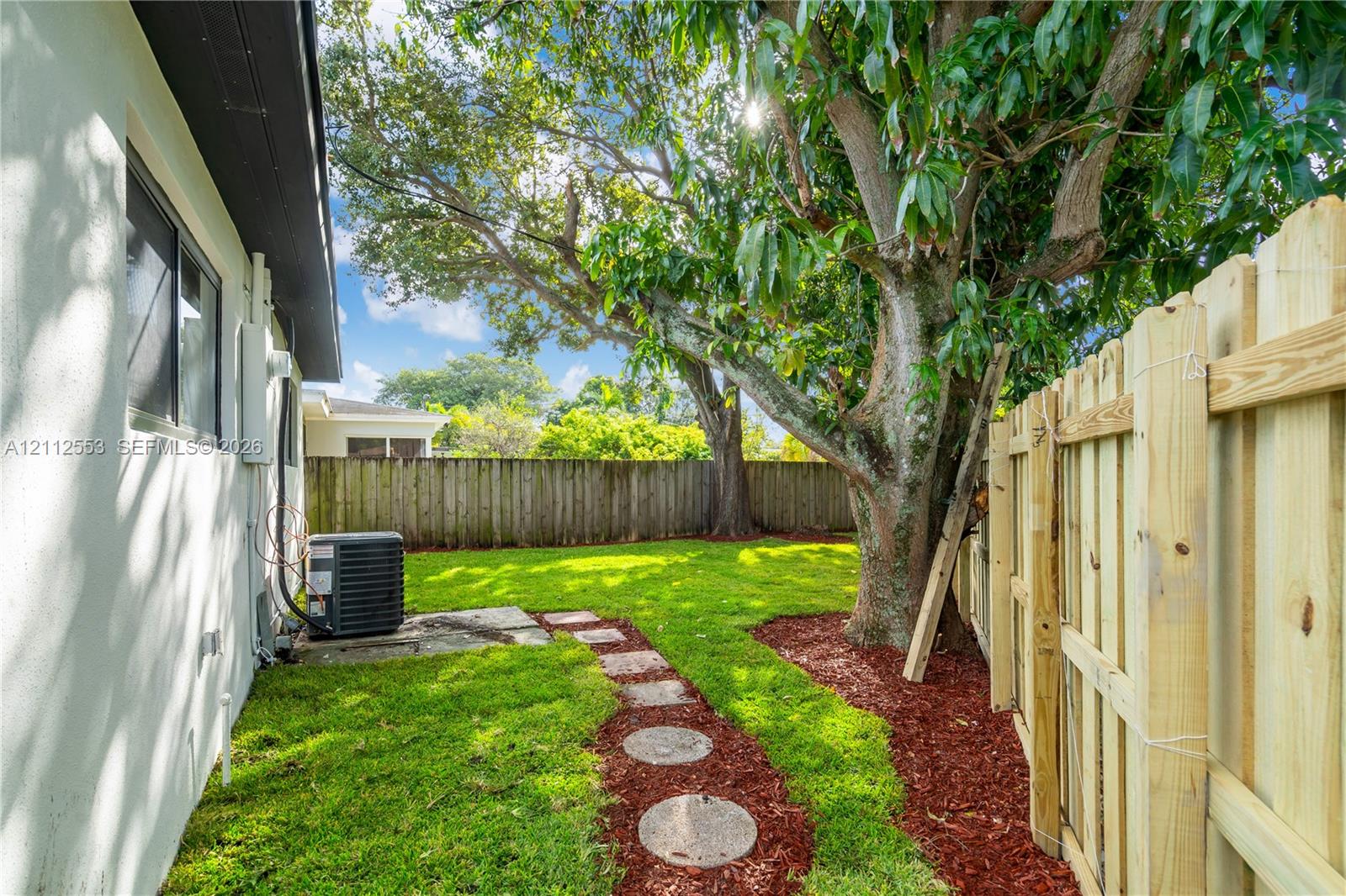 Private backyard featuring a manicured lawn, wood-finish privacy fencing, and mature trees with mulch-bordered landscaping