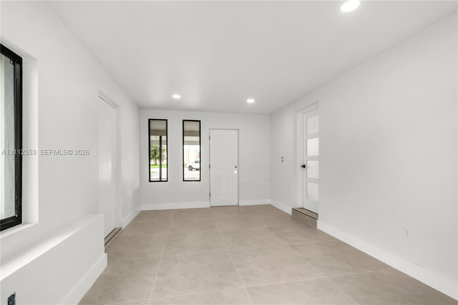 Neutral-toned large-format tile flooring, recessed ceiling lighting, multi-pane glass entry door, and vertical windows with black frames
