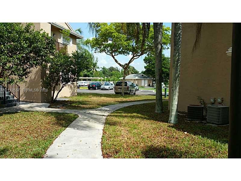 Exterior grounds featuring concrete walkways, mature trees, and stucco building facades