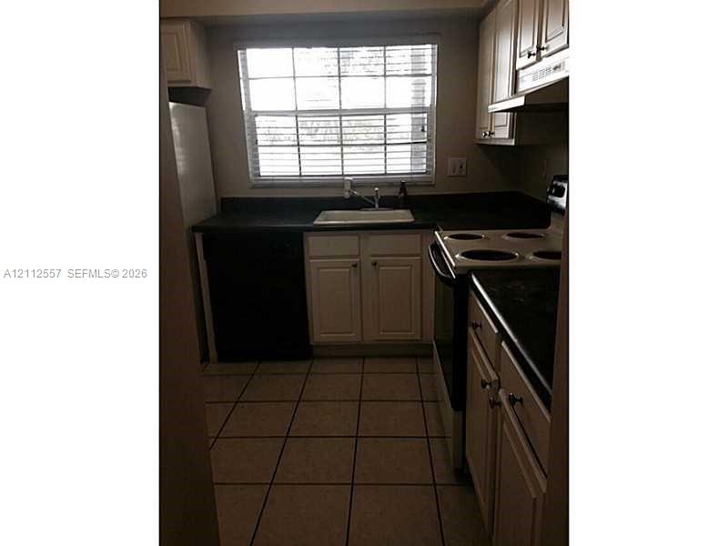 Kitchen featuring light-toned cabinetry, dark solid-surface countertops, tile flooring, and a window above a drop-in sink