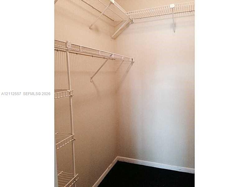 Walk-in storage space featuring white wire shelving units and dark flooring