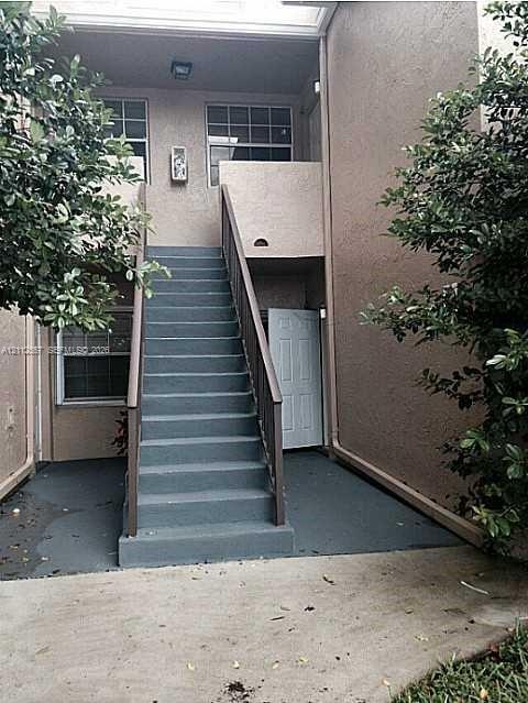 Stucco exterior featuring an enclosed staircase with painted concrete treads and metal handrails, leading to a recessed entry with a paneled door and multi-light windows