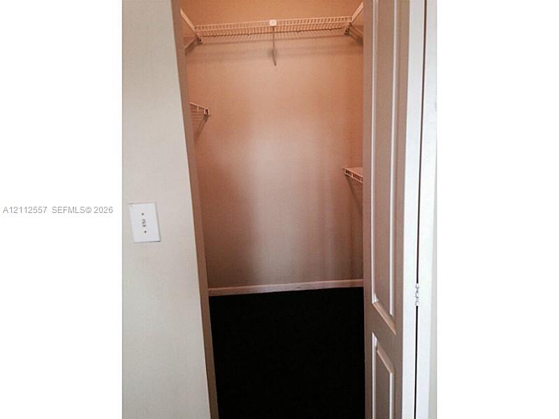 Walk-in storage space featuring white wire shelving and dark flooring