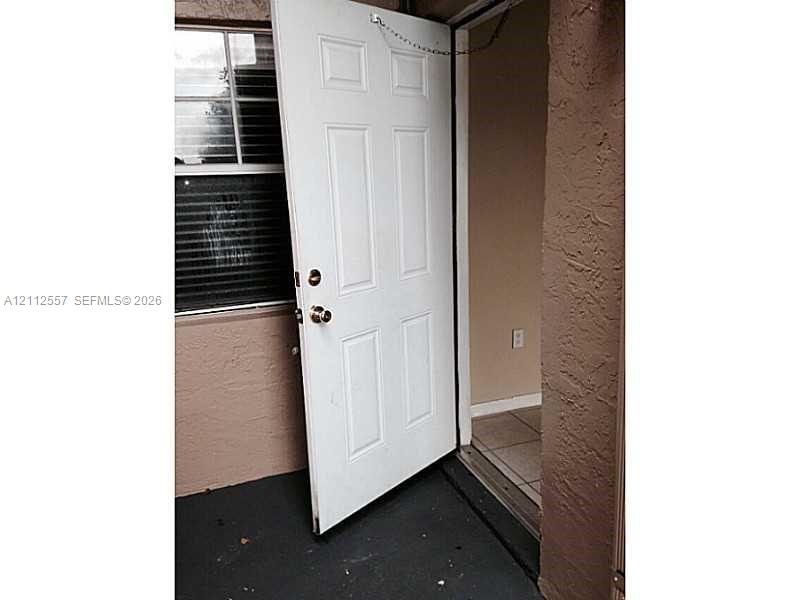 White six-panel entry door with metallic hardware, exterior stucco finish, and window featuring horizontal blinds