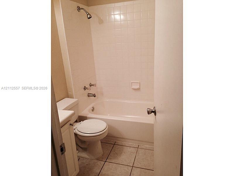 Full bathroom featuring a tub-shower combination with tiled surround, white vanity, ceramic tile flooring, and integrated shower fixtures