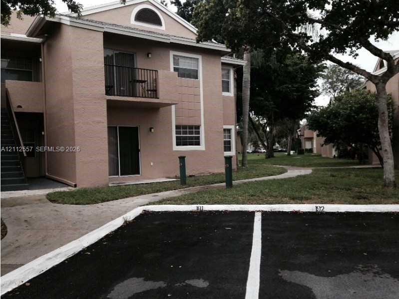 Multi-story exterior featuring a stucco facade, arched gable window, upper-level balcony with metal railing, and dedicated asphalt parking spaces