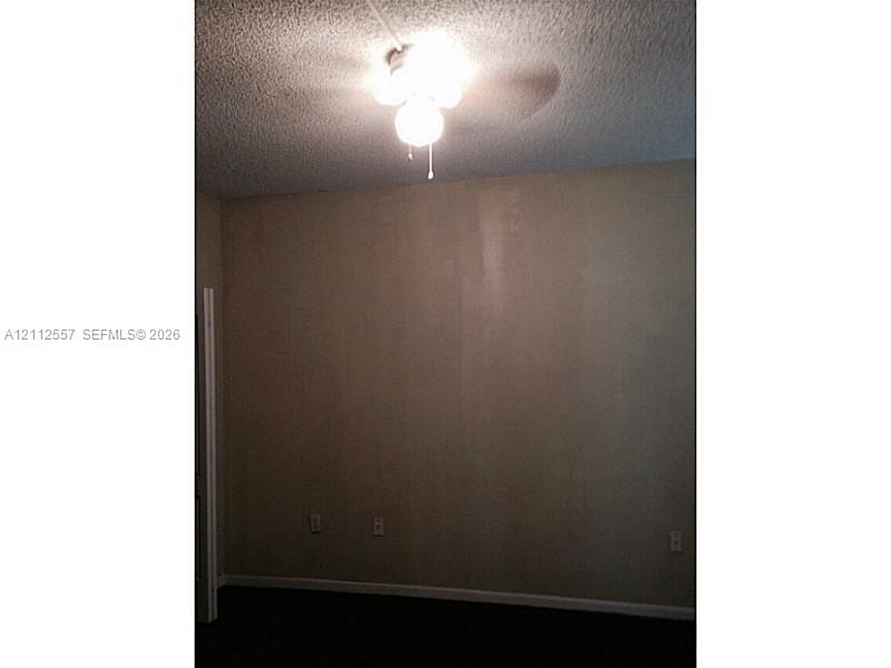 Room featuring a ceiling-mounted light fixture with a three-blade fan, textured ceiling, and doorway entrance