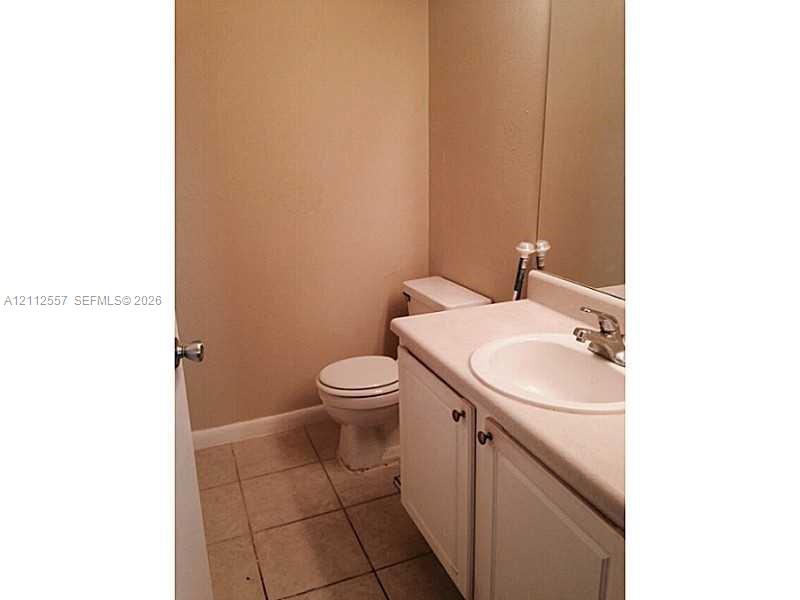 Bathroom featuring a vanity with white cabinetry, a single-basin sink, a metal faucet, a large wall-mounted mirror, and ceramic tile flooring
