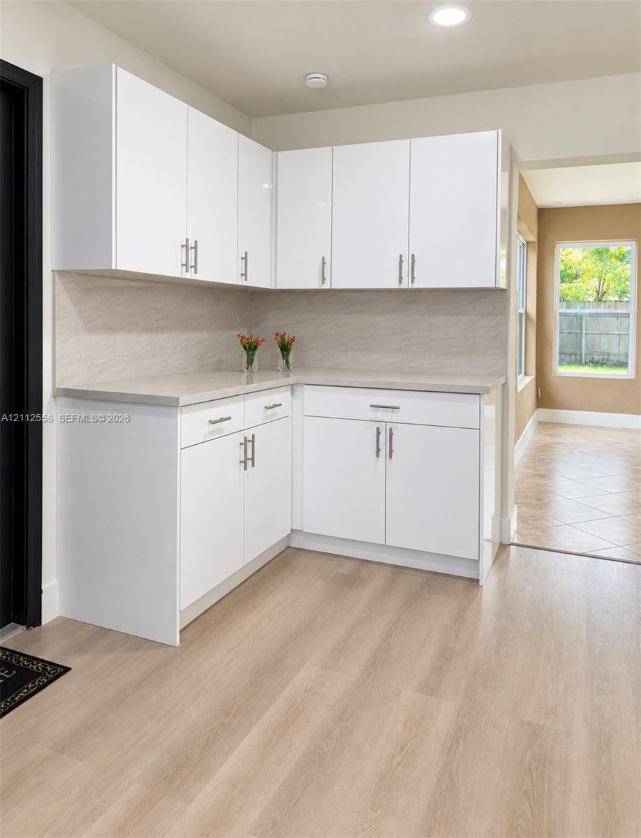 White cabinetry with brushed nickel hardware, stone-finish countertops, full-height stone-patterned backsplash, and wood-finish flooring White cabinetry with brushed nickel hardware, stone-finish countertops, full-height stone-patterned backsplash, and wood-finish flooring
