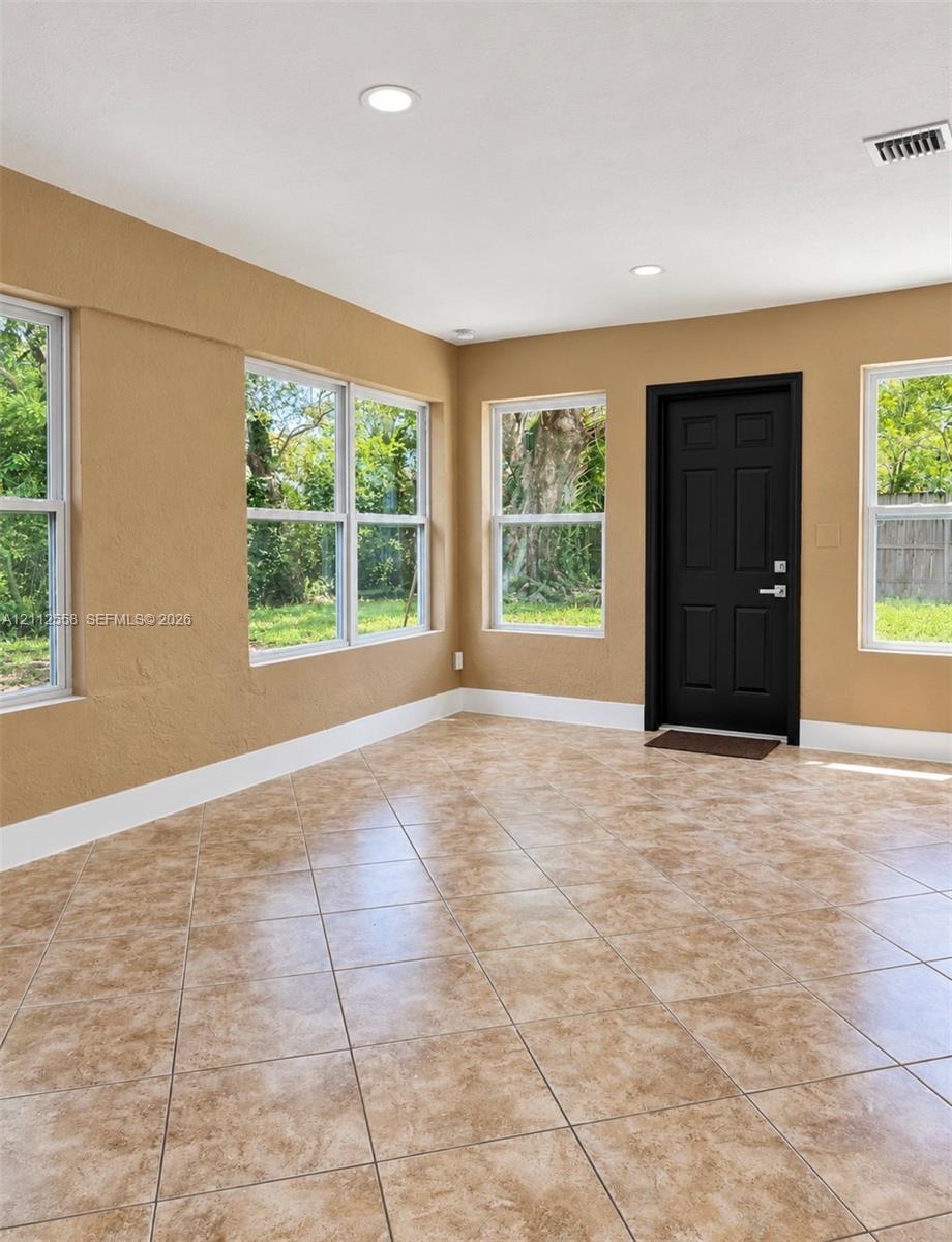 Neutral-toned interior space featuring large windows, stone-finish tile flooring, and a six-panel door with matte black hardware