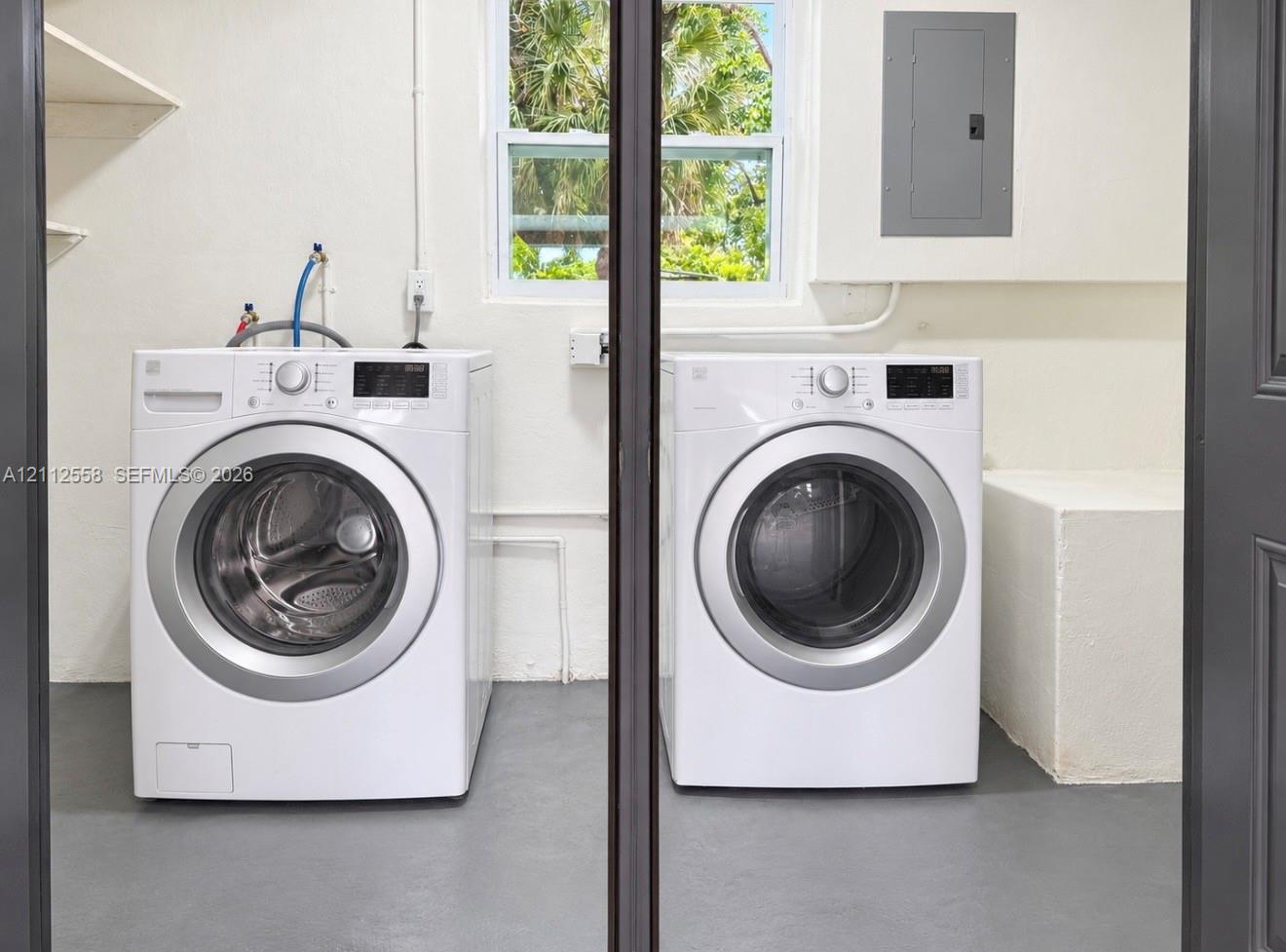 Dedicated utility space featuring built-in shelving, a single-hung window, concrete-finish flooring, and a wall-mounted electrical panel