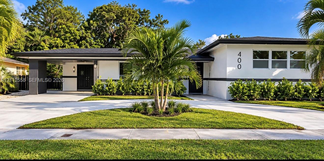 Mid-century exterior featuring a low-pitched roof, clean white stucco facade with dark trim, expansive concrete driveway, covered carport, and manicured landscaping Mid-century exterior featuring a low-pitched roof, clean white stucco facade with dark trim, expansive concrete driveway, covered carport, and manicured landscaping