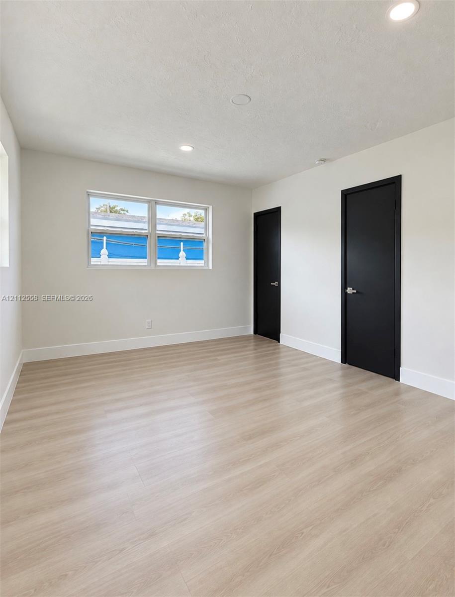 Neutral-toned interior room featuring wood-finish flooring, recessed lighting, and two solid-core doors with matte black finish hardware
