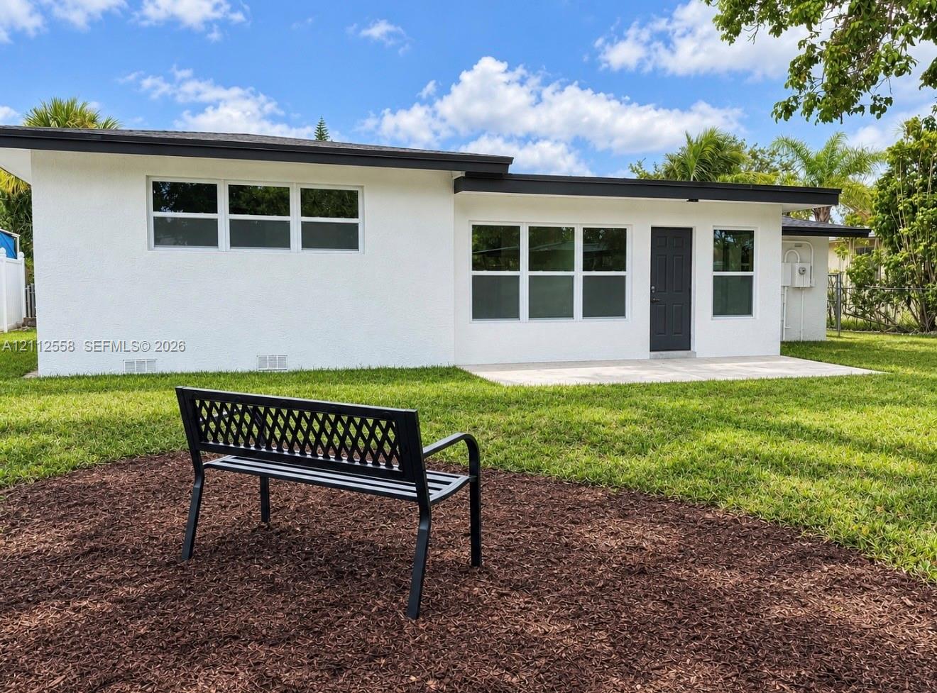 Stucco exterior featuring multi-pane windows, a dark-toned door, a paved concrete patio, and a grass lawn