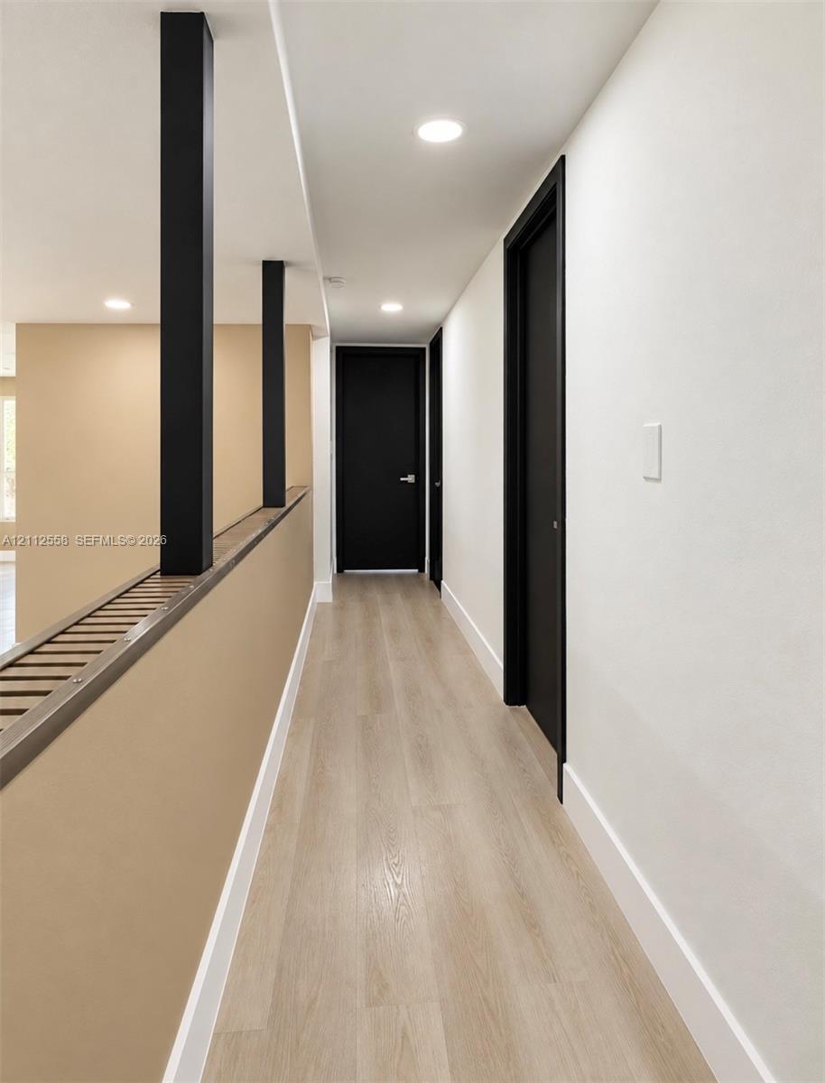 Hallway featuring wood-finish flooring, recessed lighting, matte black door frames, and high-contrast structural pillars