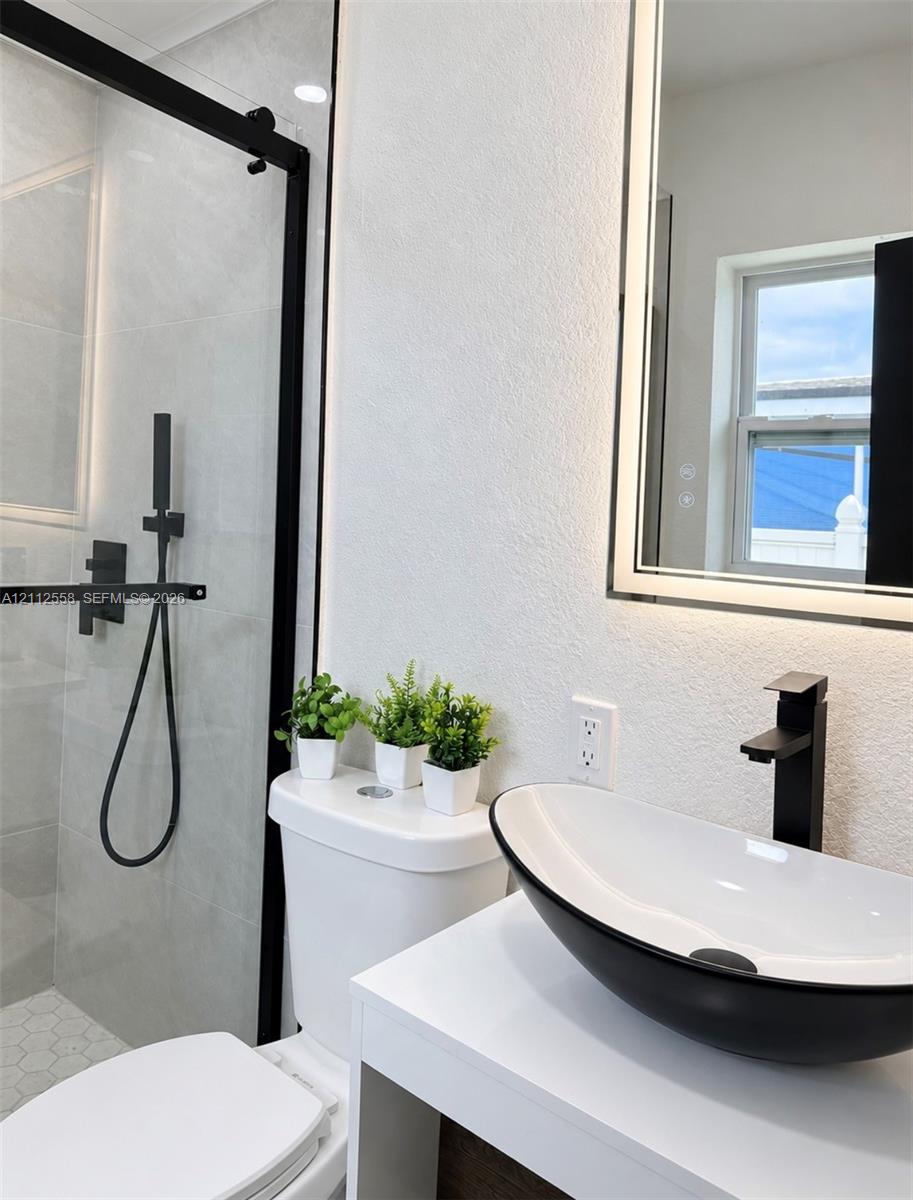 Walk-in shower with glass enclosure and matte black hardware, vanity with vessel sink, and illuminated mirror