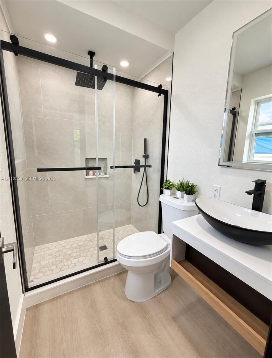 Walk-in shower with sliding black-framed glass door, large-format wall tile, integrated tile niche, and matte black rainfall showerhead