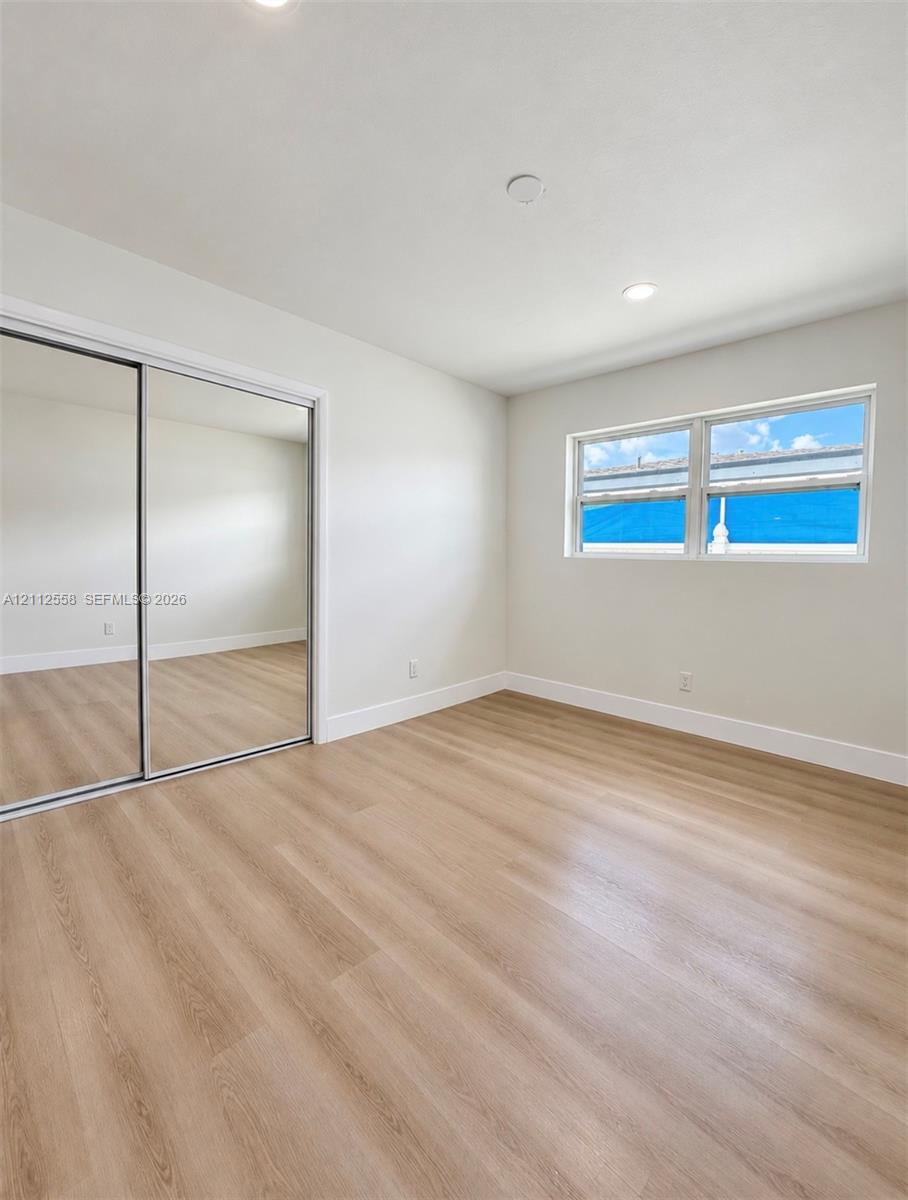Neutral-toned interior featuring wood-finish flooring, recessed lighting, and a closet with mirrored sliding doors