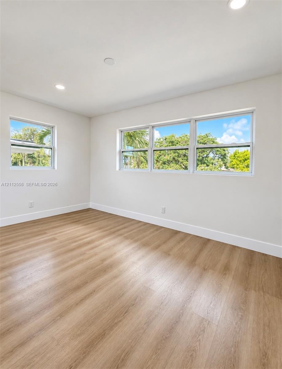 Neutral-toned interior featuring wood-finish flooring, recessed lighting, and multiple windows providing natural illumination