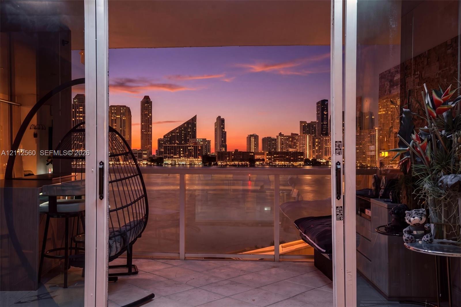Covered balcony featuring tile flooring and a glass-paneled railing, with expansive waterfront and cityscape scenery