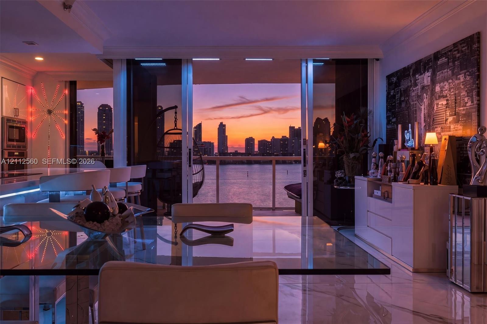 Floor-to-ceiling sliding glass doors, stone-finish flooring, built-in cabinetry, and integrated kitchen appliances, complemented by a water and cityscape backdrop