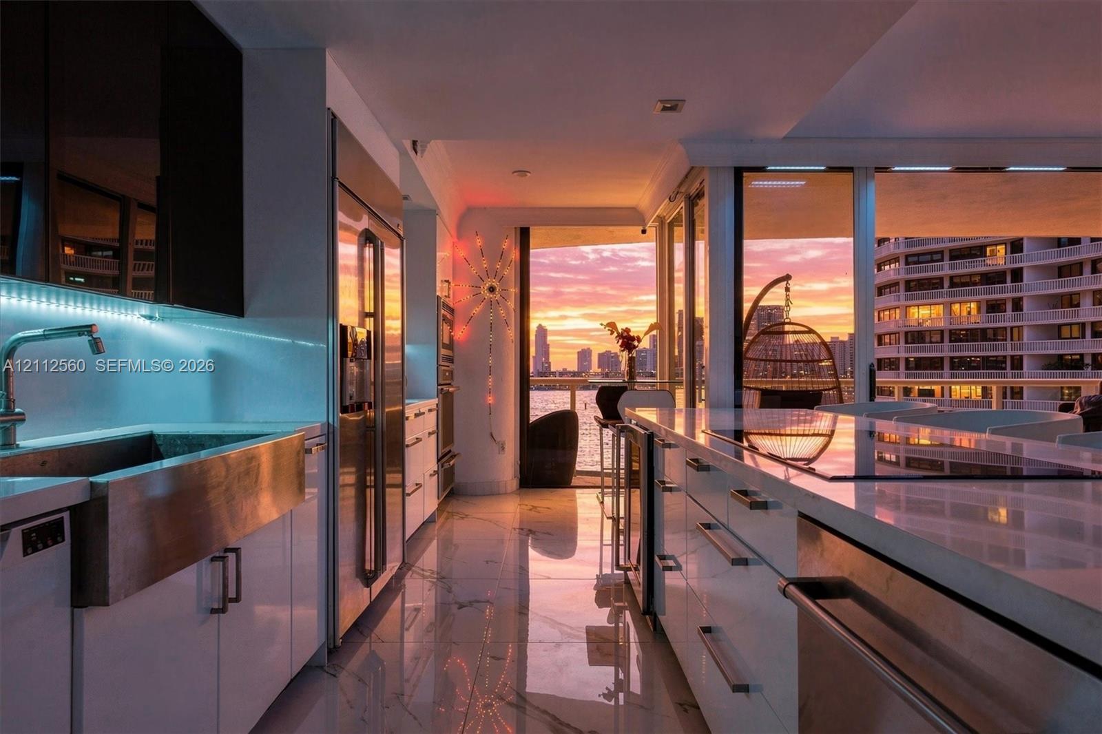 Modern kitchen featuring sleek white cabinetry, stainless steel apron-front sink, polished stone countertops, integrated stainless steel appliances, and large-format tile flooring