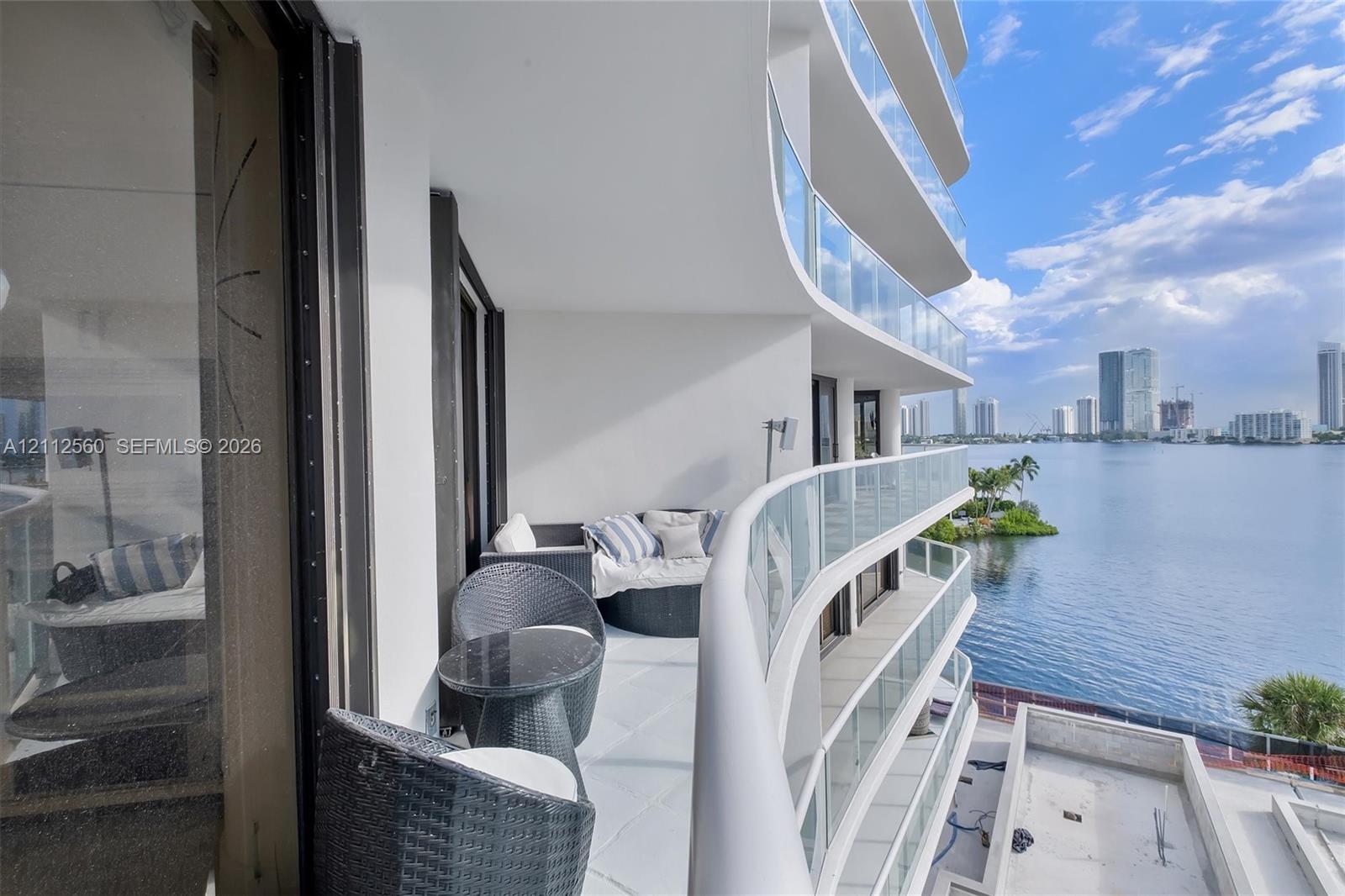 Curved wrap-around balcony featuring glass panel railings, white flooring, and wide-reaching water frontage