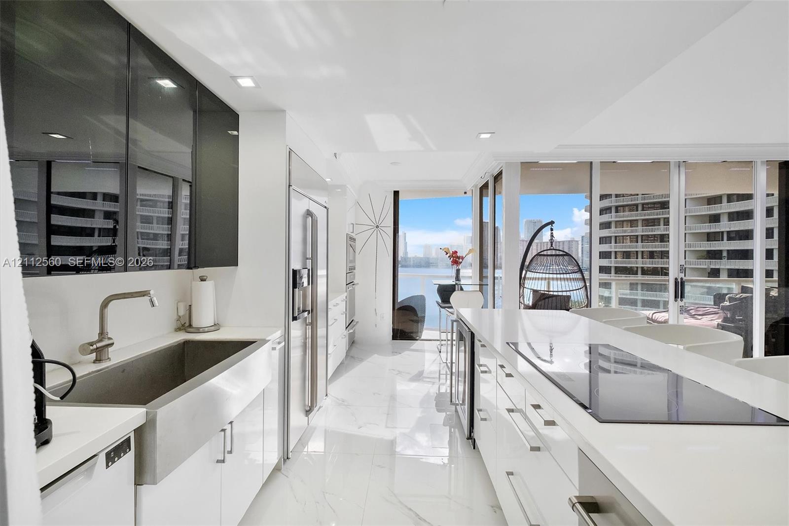 Kitchen featuring high-gloss cabinetry, stainless steel farmhouse sink, white stone-surfaced countertops, built-in appliances, and floor-to-ceiling windows