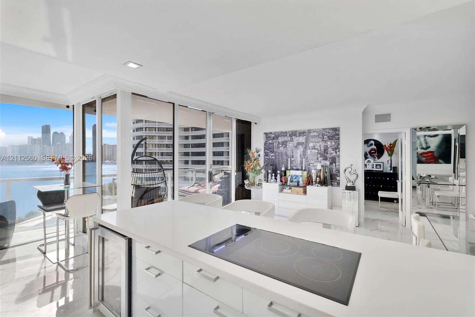 Open-concept kitchen featuring an island with a quartz countertop, an integrated glass cooktop, a built-in under-counter beverage refrigerator, and floor-to-ceiling glass panel walls