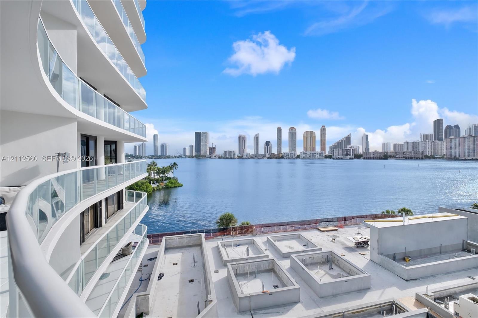 Curved exterior balconies with glass railings overlooking a large body of water and an urban skyline