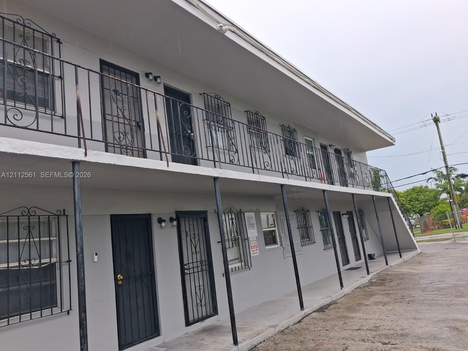 Two-story exterior featuring a neutral painted facade, metal security bars on windows and doors, covered concrete walkways, and an integrated staircase