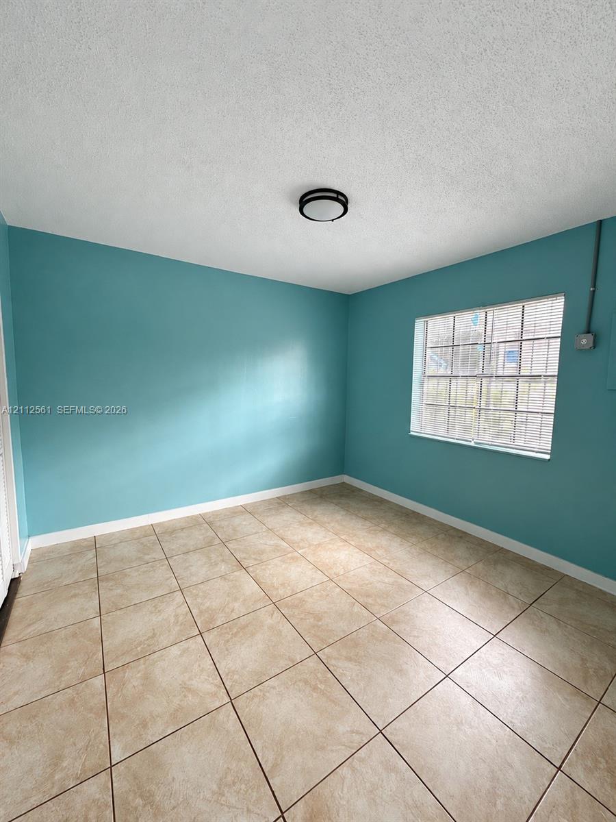 Interior room featuring large-format ceramic tile flooring, a multi-pane window with blinds, and a flush-mount circular ceiling light fixture