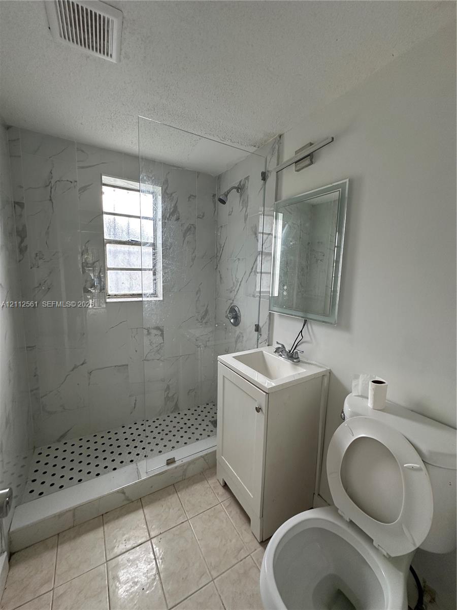 Walk-in shower with floor-to-ceiling stone-finish tile surround and glass partition, basketweave-pattern tile shower floor, and a single-basin vanity cabinet