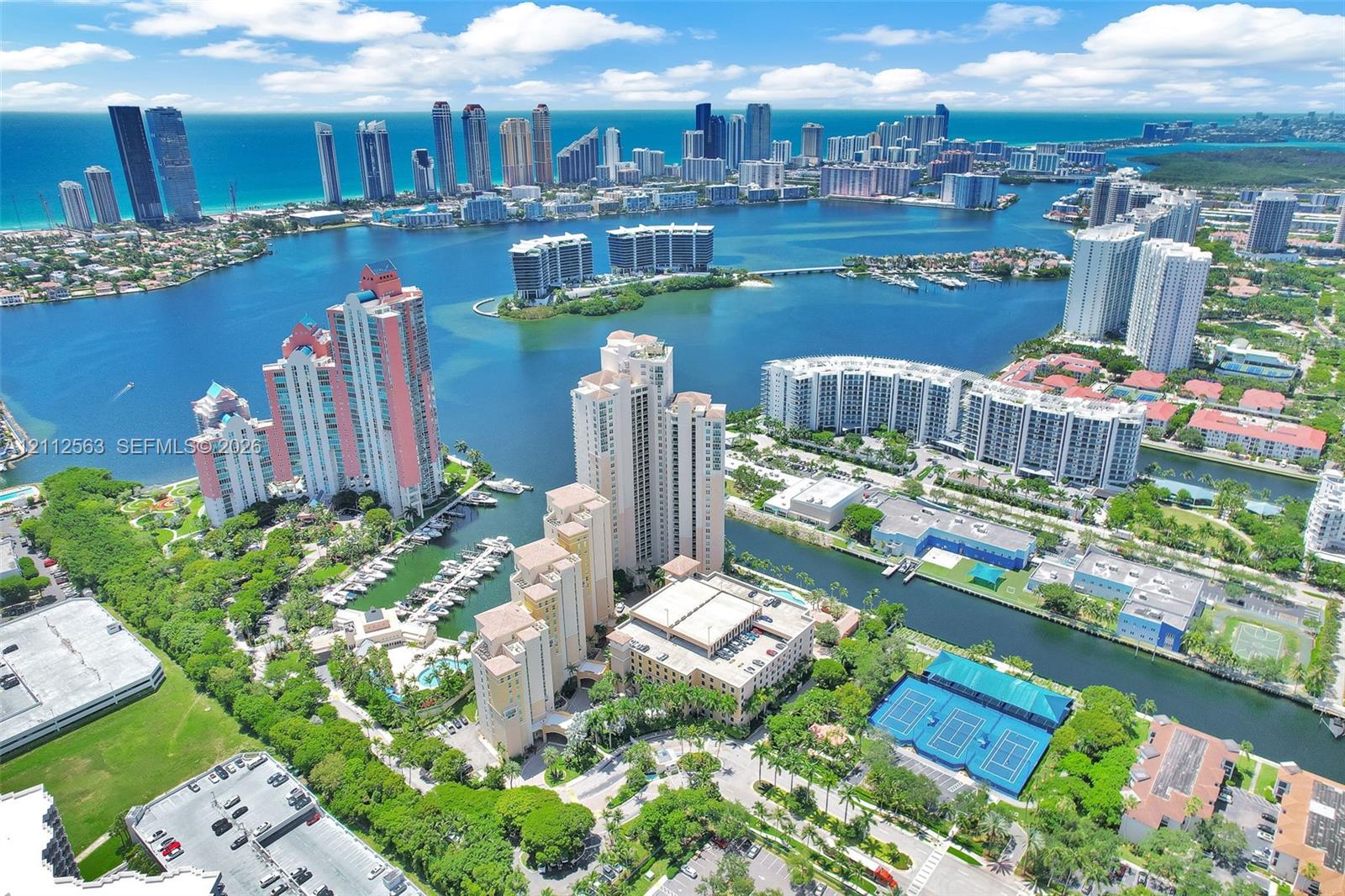 Aerial perspective featuring waterfront high-rise residential towers, private marina slips, hard-court tennis facilities, and expansive coastal waterways