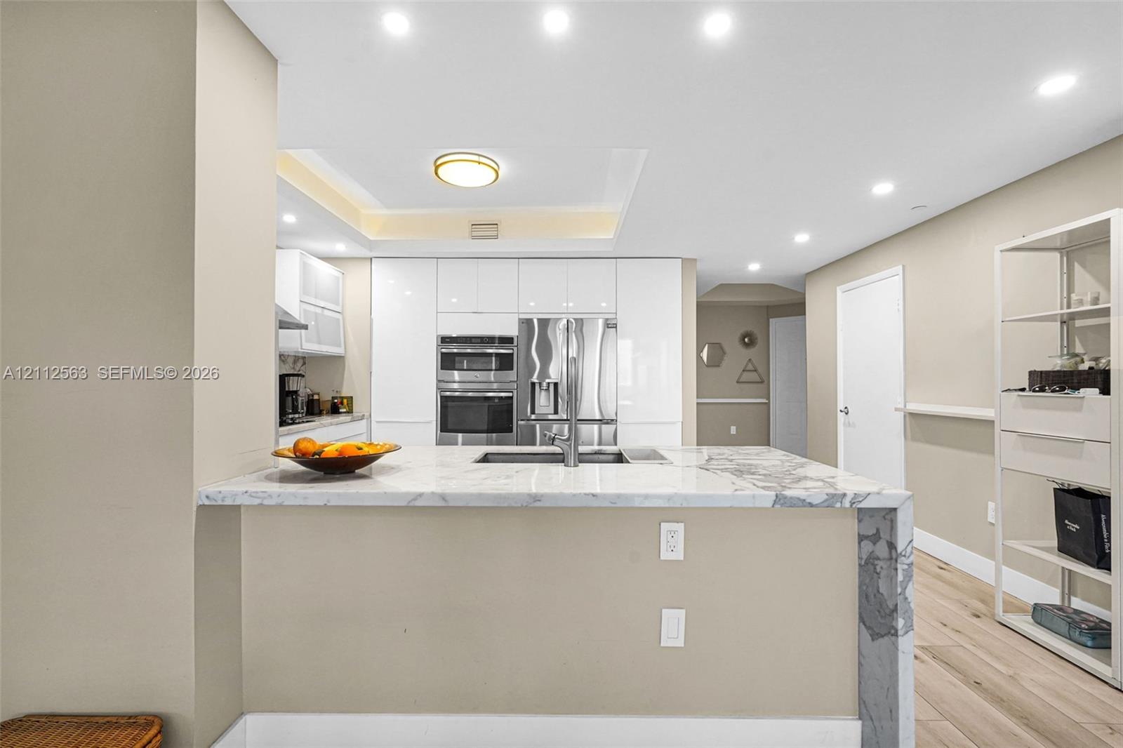 Kitchen featuring white slab-front cabinetry, a waterfall-edge stone island, integrated stainless steel appliances, recessed lighting, and wood-finish flooring