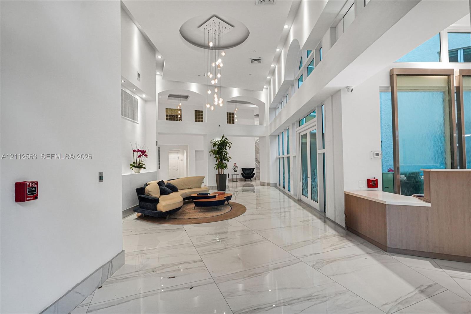 Grand foyer featuring double-height ceilings, stone-finish flooring, floor-to-ceiling windows, arched architectural details, and a tiered modern chandelier