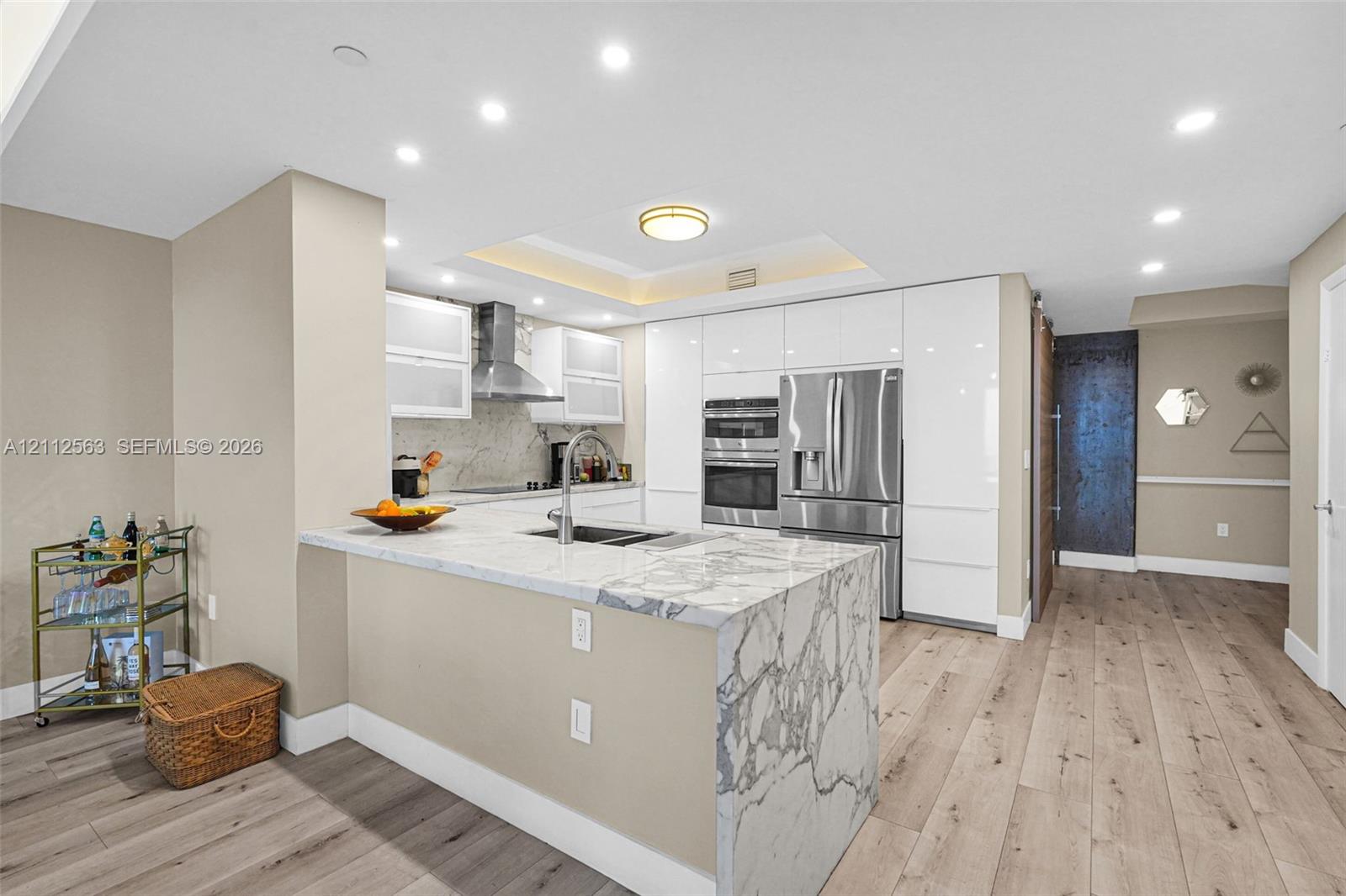 Kitchen featuring stone-finish waterfall edge countertops, gloss-finish cabinetry, built-in stainless steel double wall ovens, recessed ceiling lighting, and wood-finish flooring