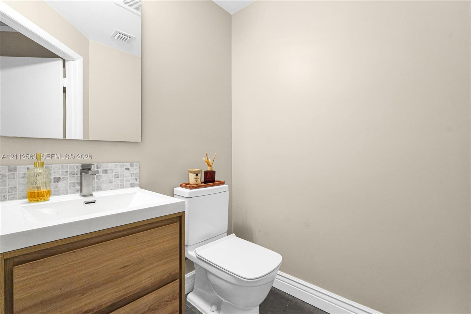 Vanity featuring a wood-finish cabinet with an integrated white sink, rectangular frameless mirror, and a mosaic tile backsplash