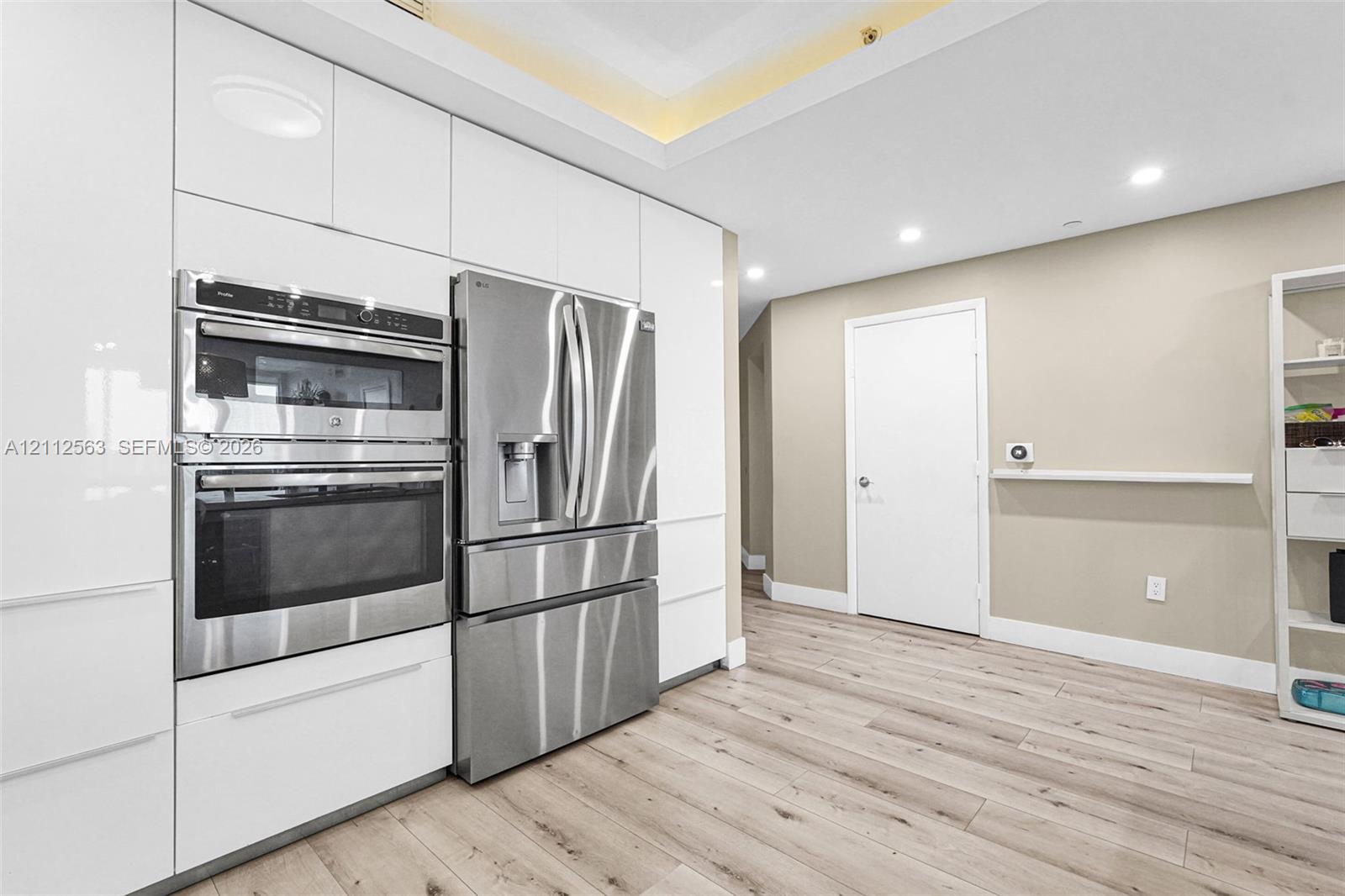 High-gloss white cabinetry, integrated stainless steel double wall ovens, French door stainless steel refrigerator, recessed lighting, and wood-finish flooring